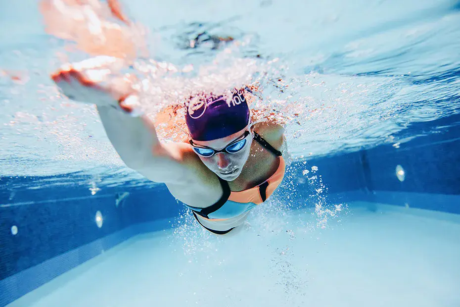 Underwater view of an adult swimmer in a purple cap and goggles powering forward with a front‑crawl stroke.