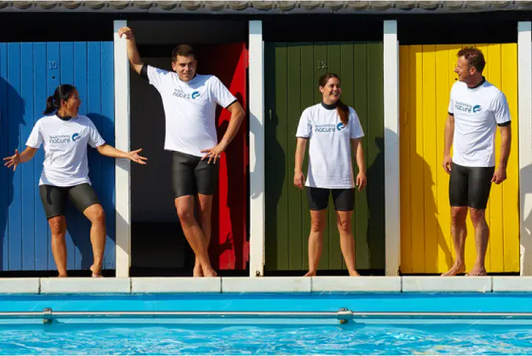 Video thumbnail showing two instructors smiling while standing poolside next to a group of swimmers entering the water.