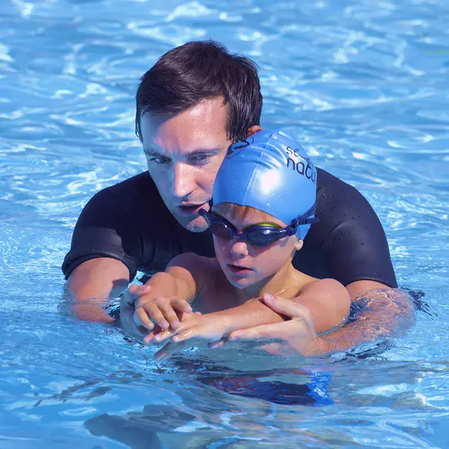 Male Swimming Nature instructor supports a child swimmer in the water, guiding them with hands-on instruction.