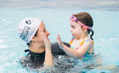 Female Swimming Nature instructor and child swimmer exchange a high-five while standing together in the pool.