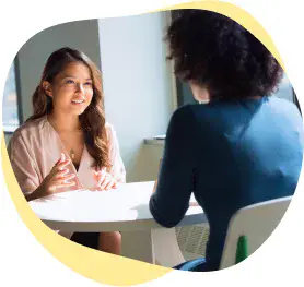 Smiling female interviewer sits at a desk speaking with an instructor candidate.
