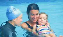 Swim instructor and parent smiling while supporting a baby in the pool.
