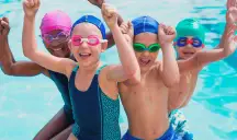 Group of children in bright swim caps cheering together at swim practice.