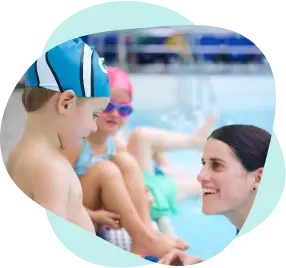 Young boy in a teal swim‑cap concentrates pool‑side while a girl in pink goggles waits her turn behind him.