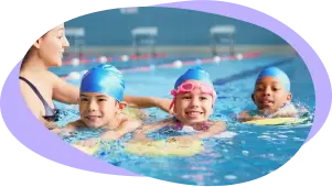 Instructor leads three children in blue caps swimming in a line, copying each other’s strokes.